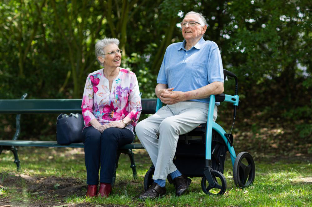 Senior couple sitting together outdoors, one using a mobility walker
